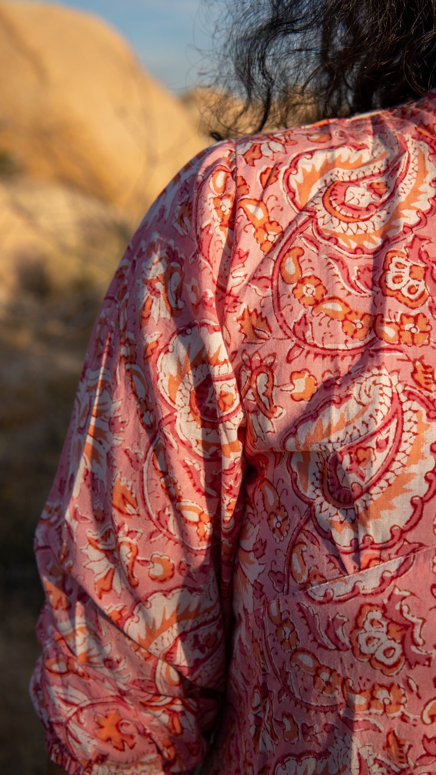 Person wearing a pink and orange patterned garment in a desert setting