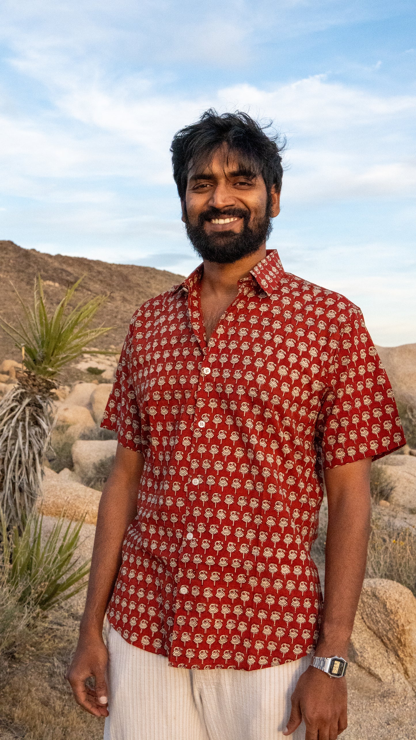 Man wearing a red patterned shirt standing in a desert landscape