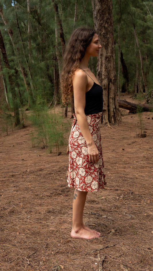 Woman standing in a forest wearing a black top and floral skirt.