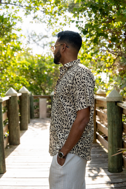 Man wearing a patterned shirt and sunglasses on a wooden bridge with greenery in the background