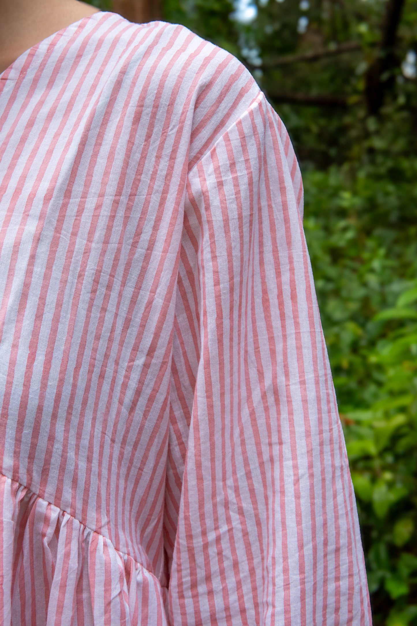 Close-up of a person wearing a pink and white striped shirt with a blurred green background