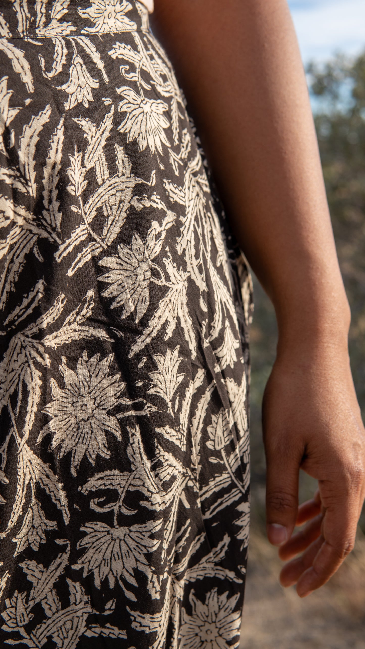 Close-up of a person wearing a black dress with white floral pattern outdoors.
