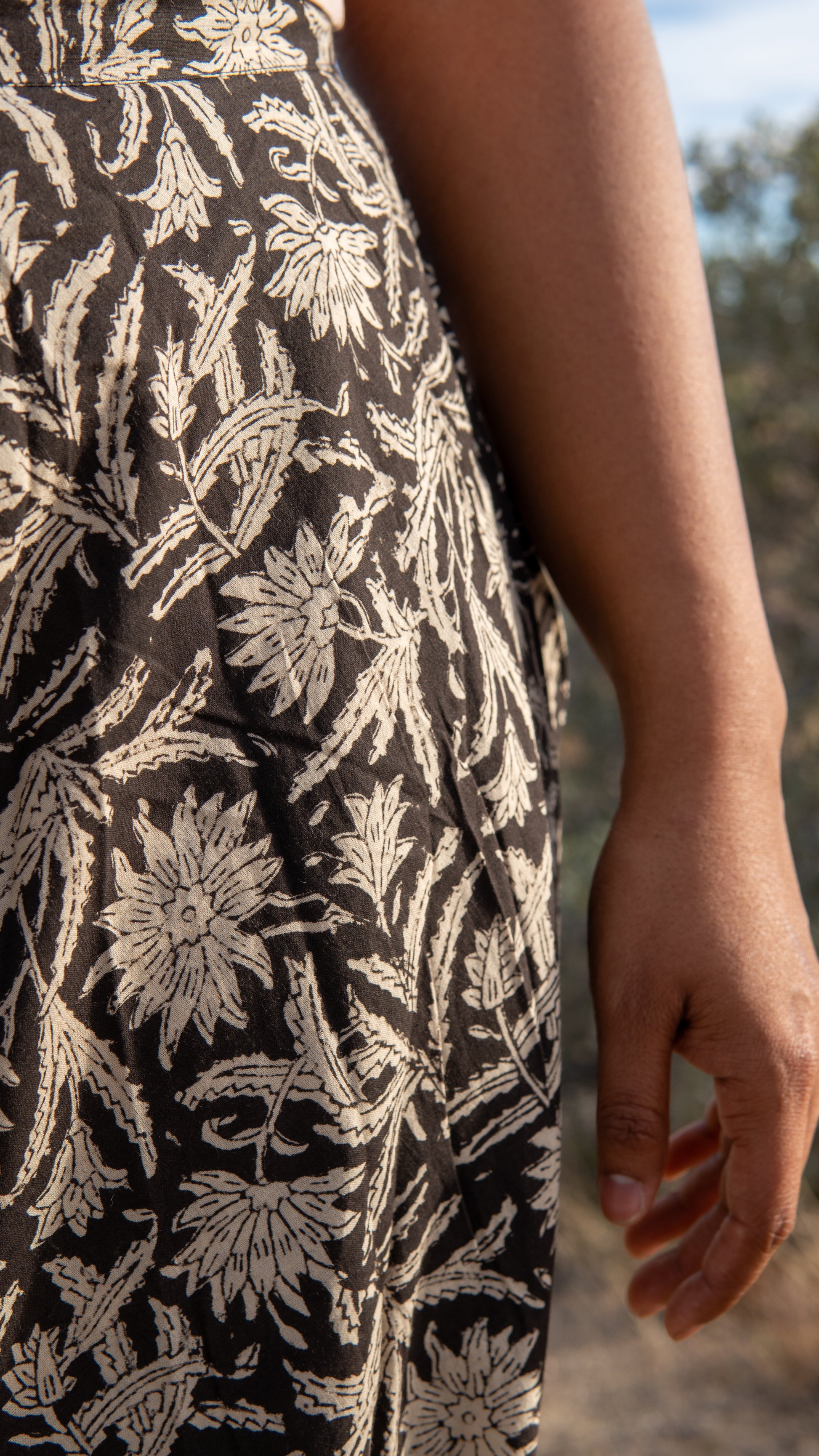 Close-up of a person wearing a black dress with white floral pattern outdoors.