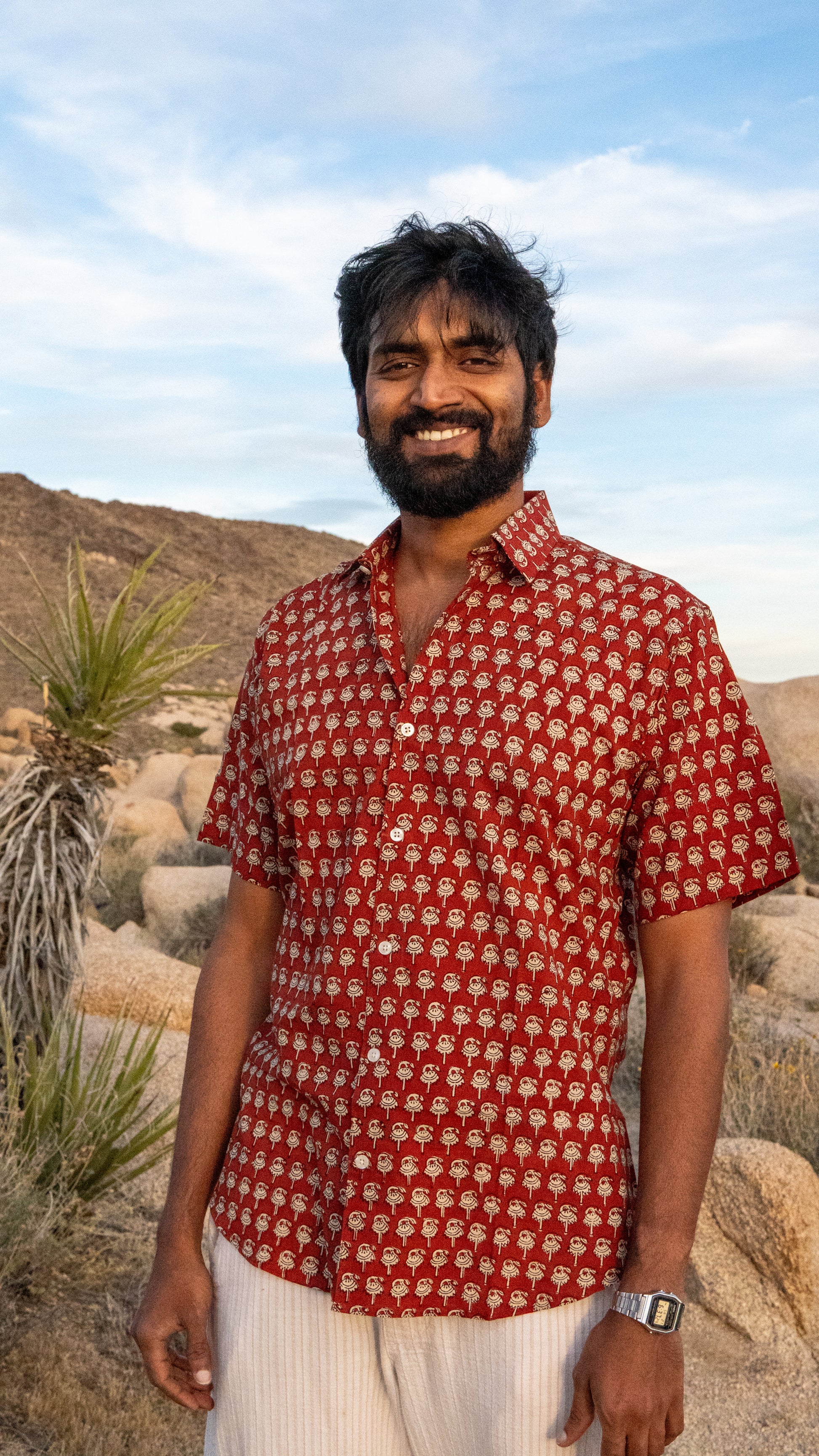 Man wearing a red patterned shirt standing in a desert landscape