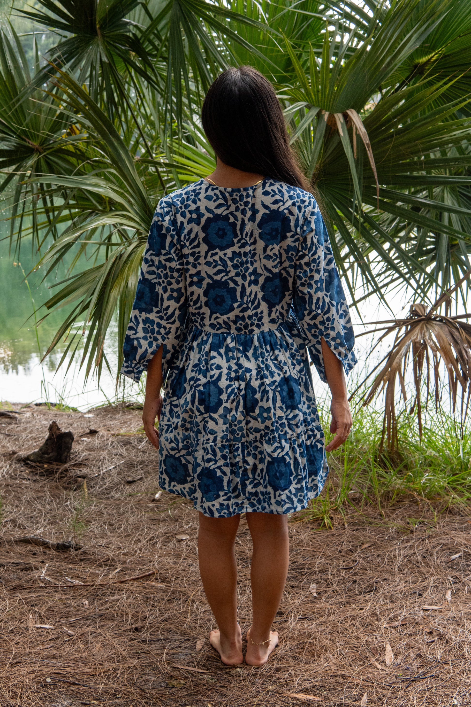 Woman in a blue floral dress standing in front of palm trees