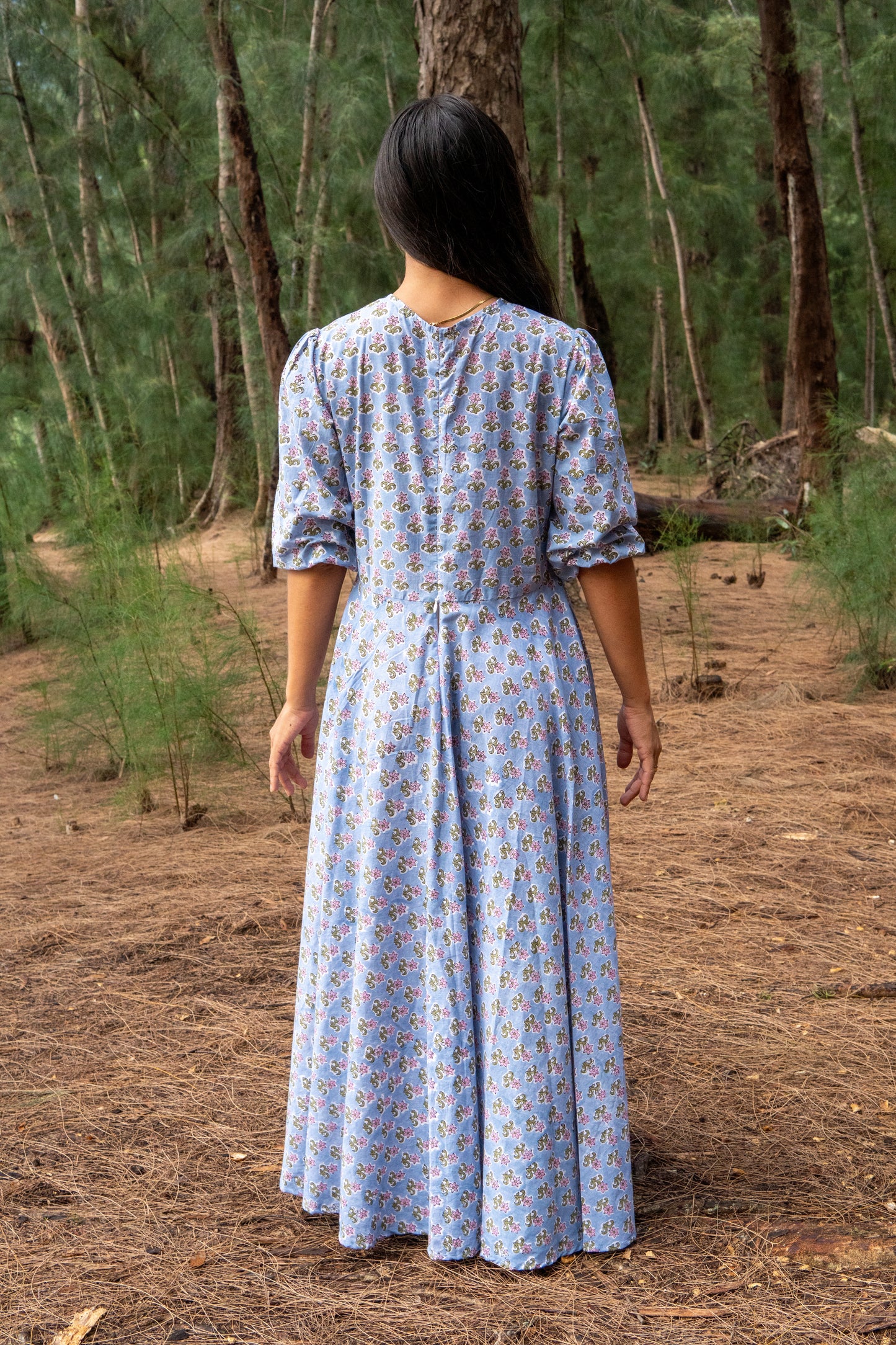 Woman in a blue patterned dress walking through a forest
