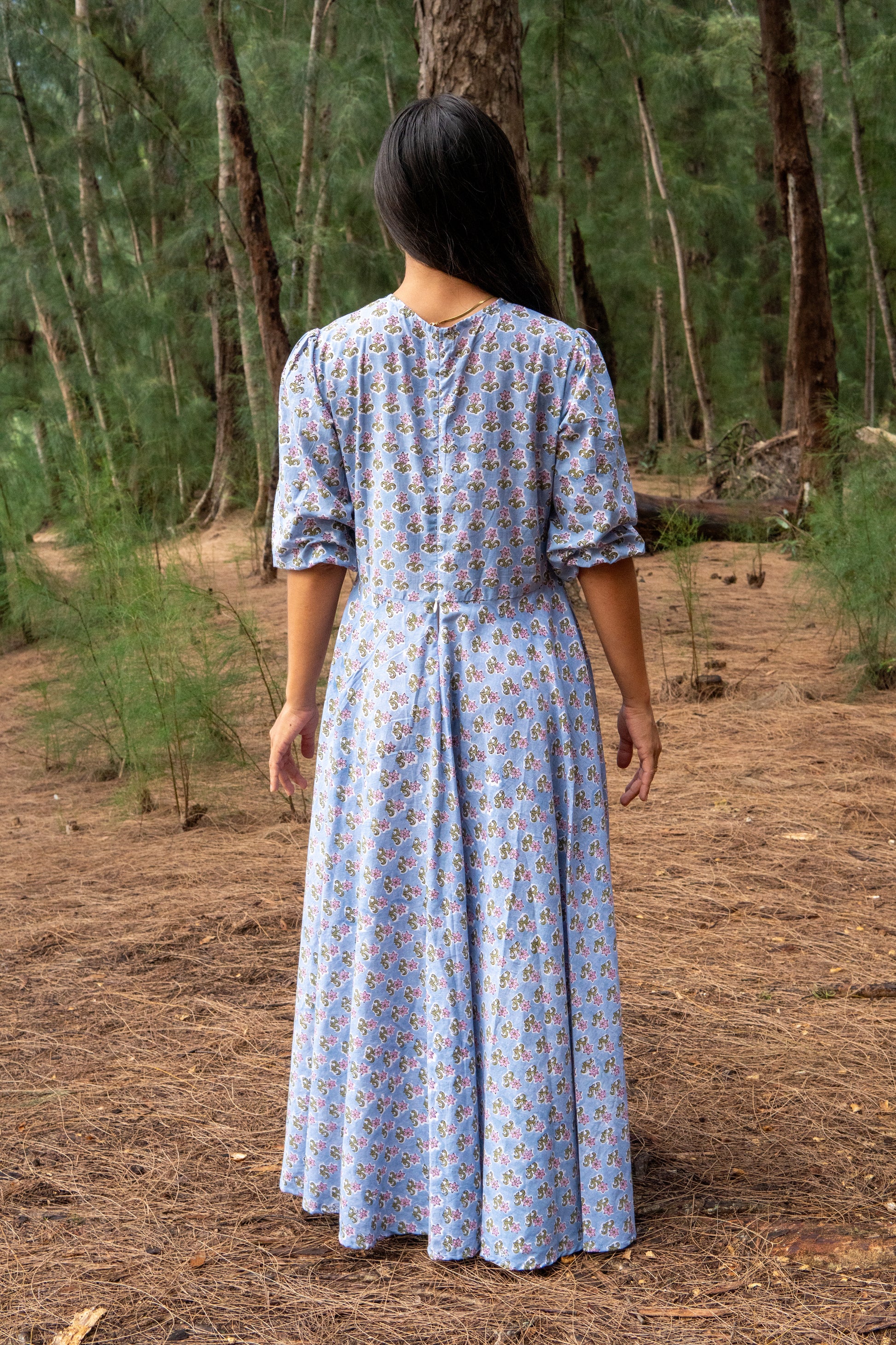 Woman in a blue patterned dress walking through a forest