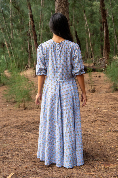Woman in a blue patterned dress walking through a forest