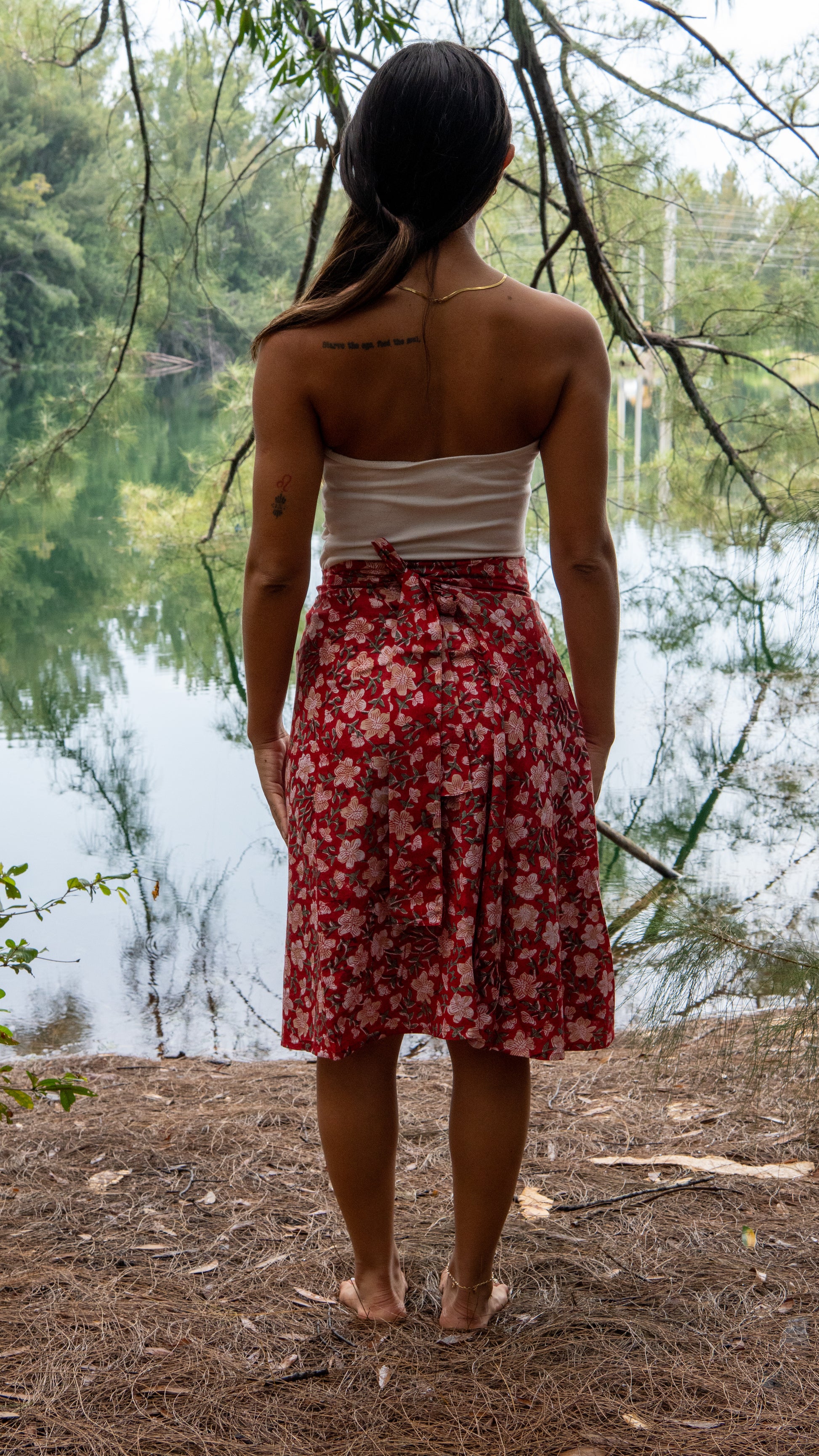 Woman in a red floral skirt standing by a lake