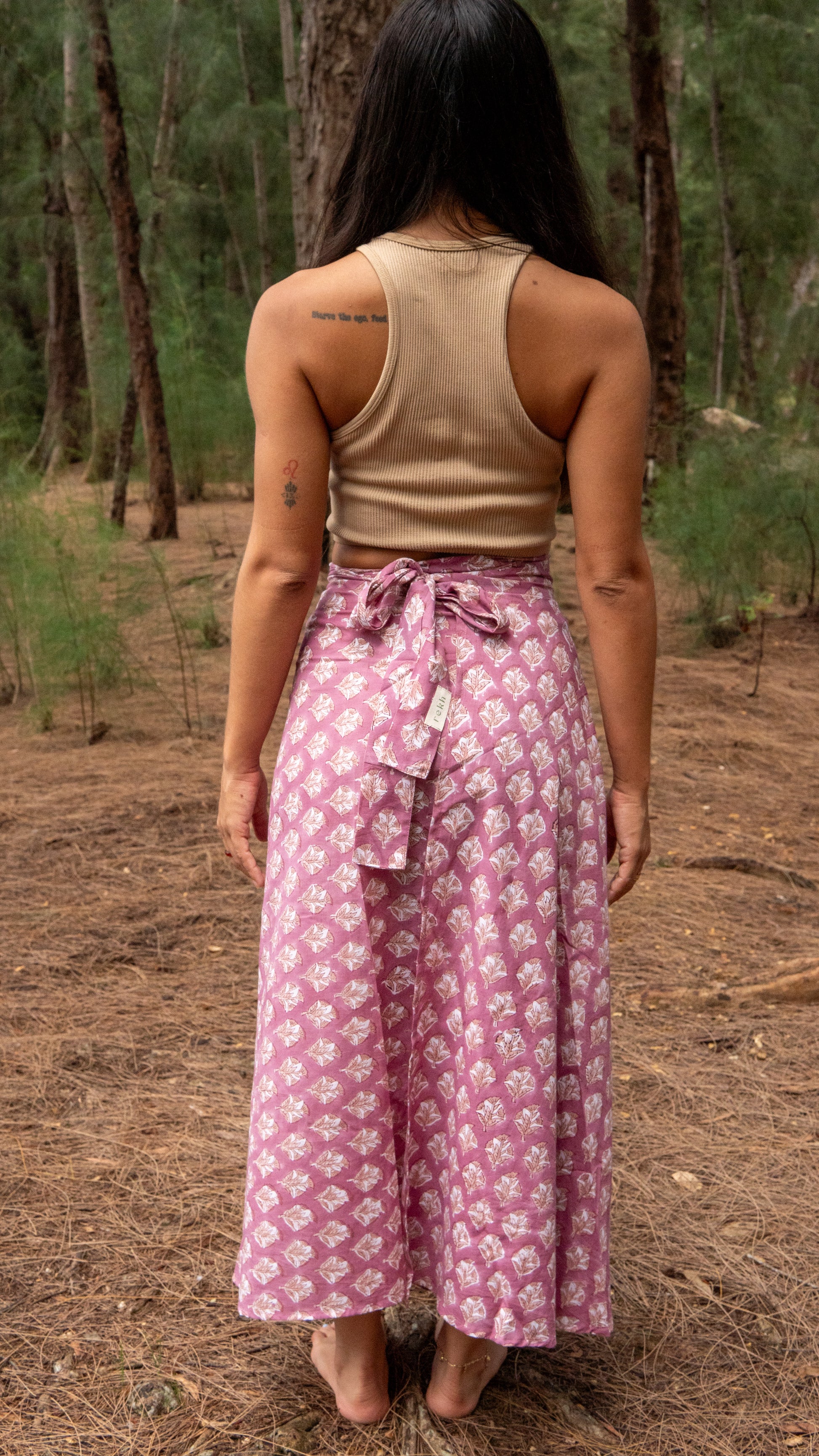 Person wearing a beige tank top and pink floral skirt in a forest setting
