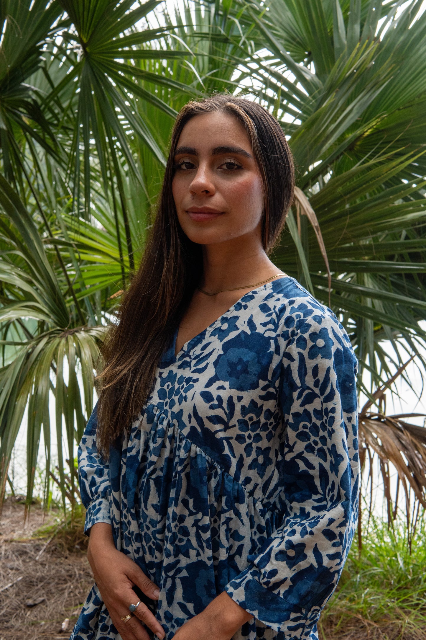 Woman in a blue and white patterned dress standing in front of palm trees