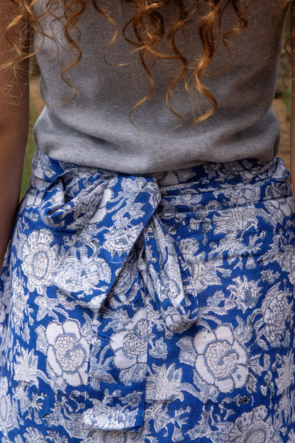 Person wearing a gray top and blue floral skirt with a blurred background