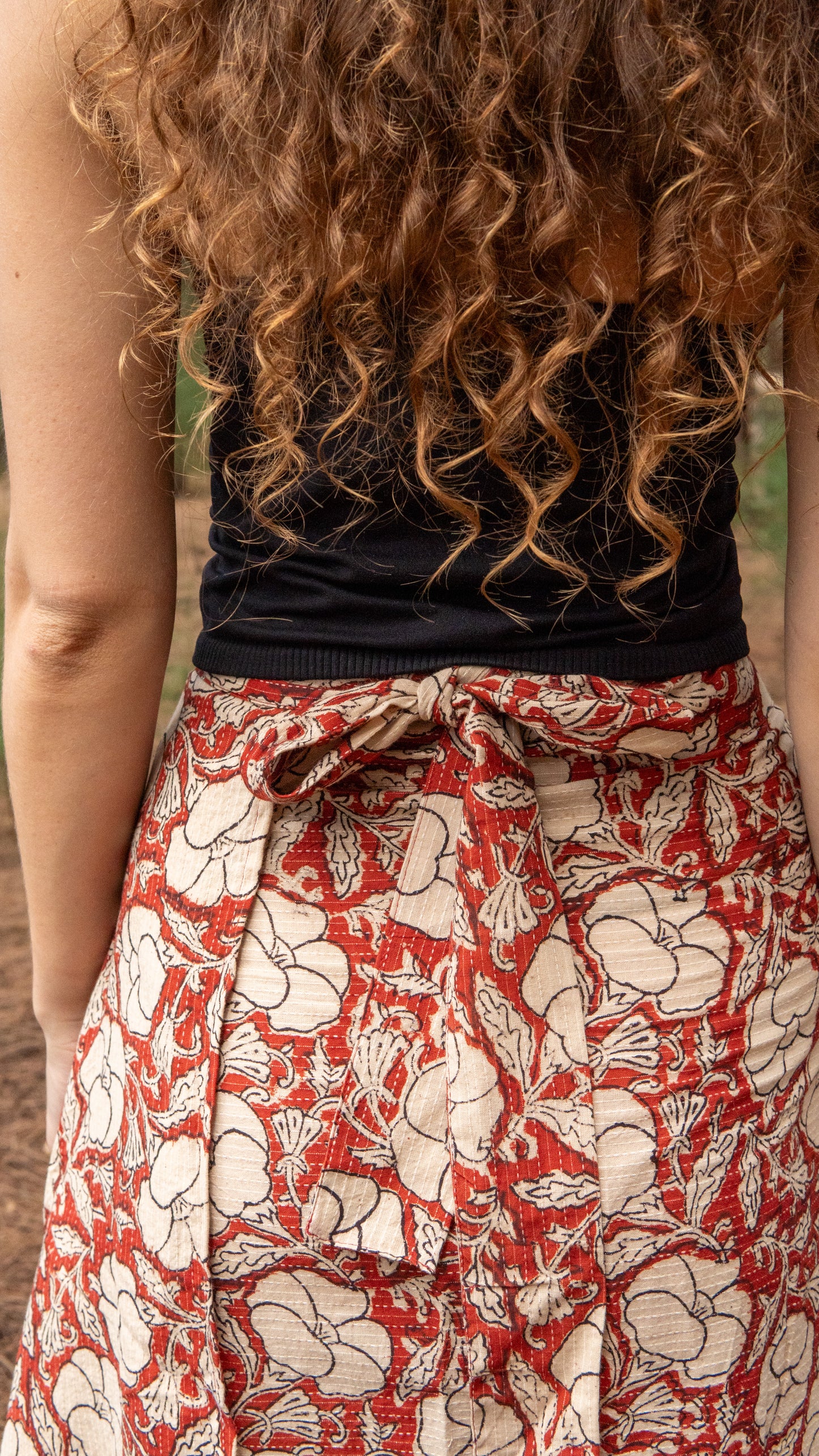 Person wearing a black top and red floral skirt with curly hair.