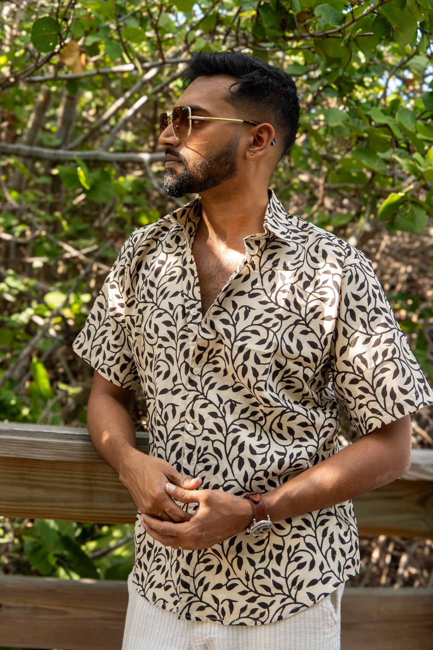 Man wearing a patterned shirt standing outdoors with greenery in the background