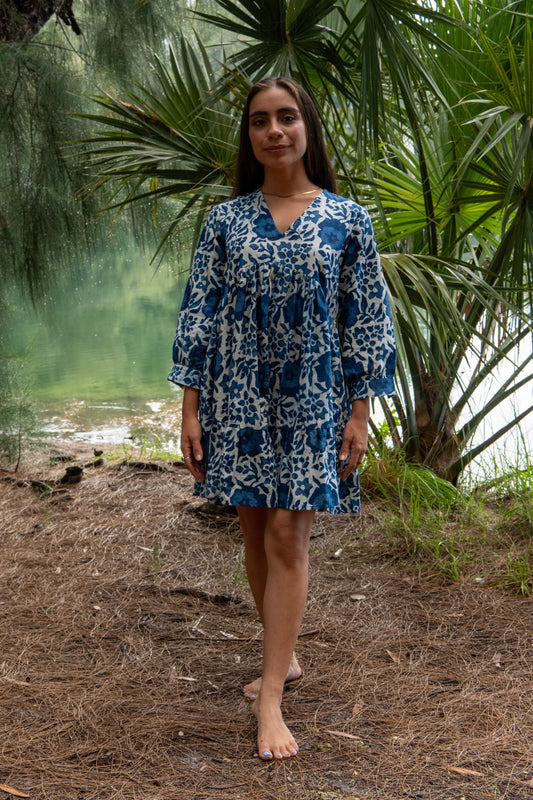 Woman in a blue floral dress standing in a natural setting with greenery.