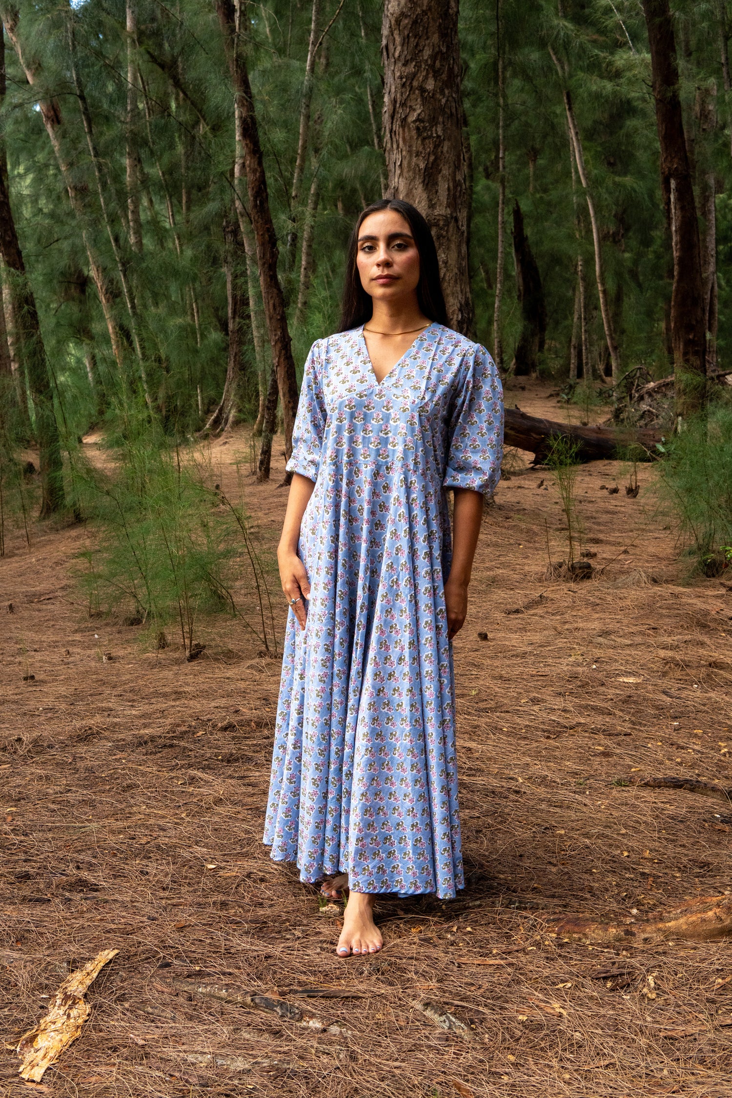 Woman in a blue patterned dress standing in a forest