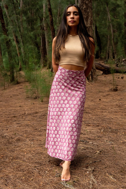 Woman in a pink patterned skirt and beige top standing in a forest