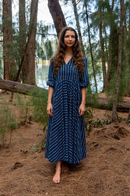 Woman in an indigo blue dress standing in a forest near a lake