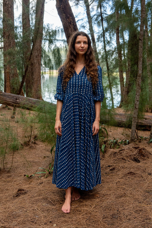 Woman in an indigo blue dress standing in a forest near a lake
