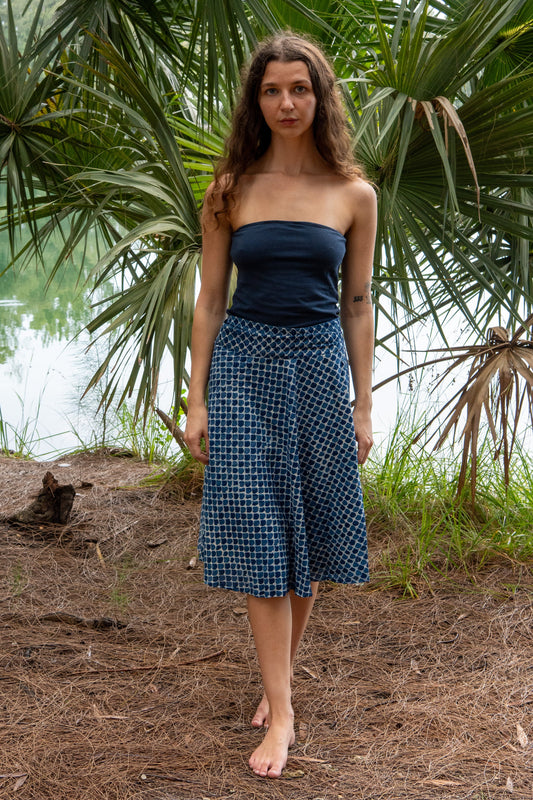 Woman wearing a blue strapless top and checkered skirt standing in a natural setting with greenery.