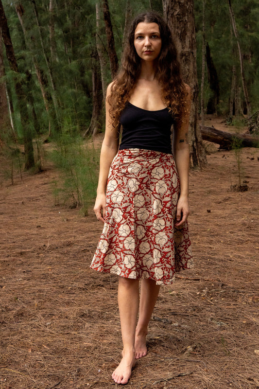 Woman standing in a forest wearing a black top and patterned skirt.