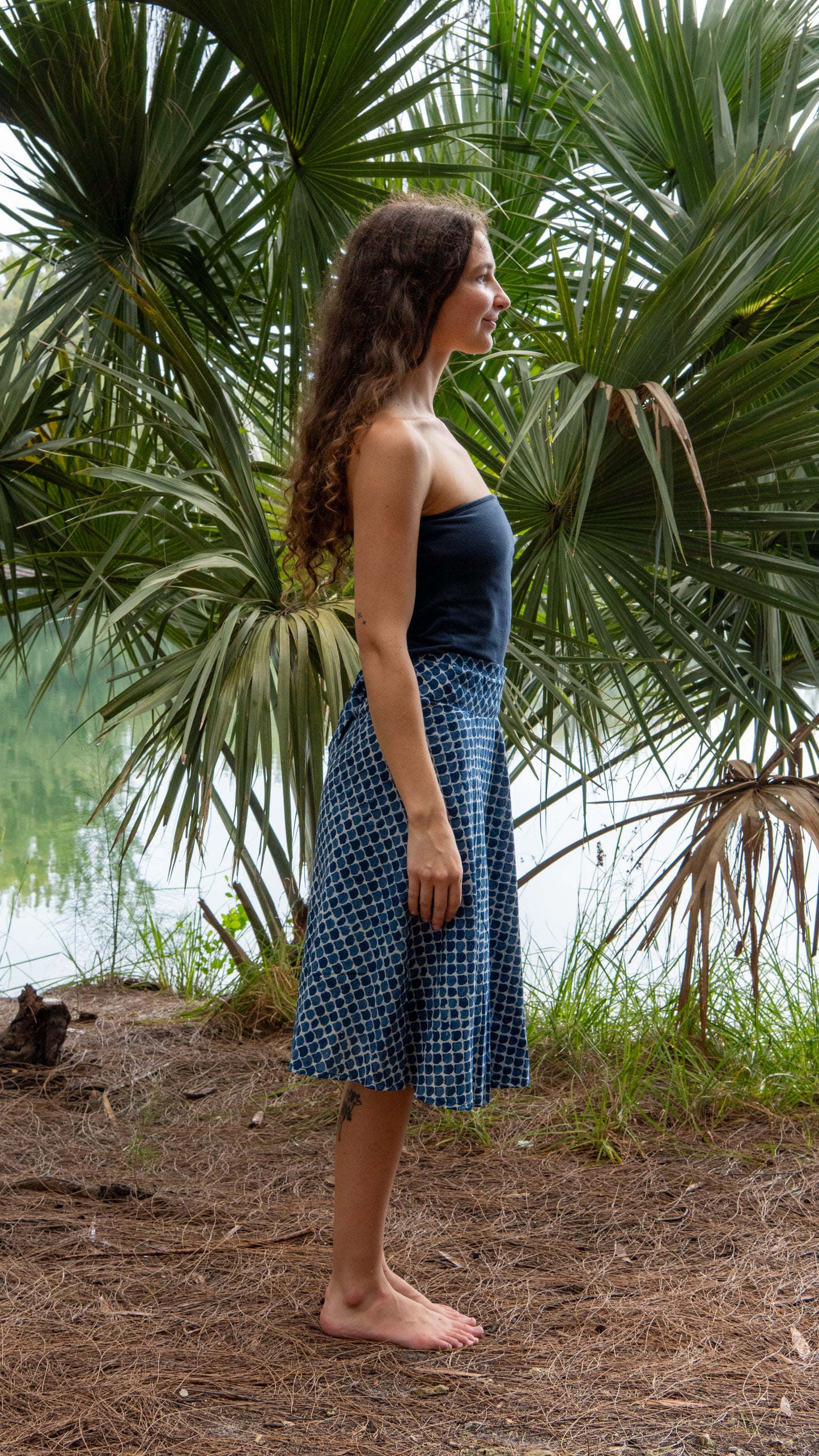 Woman in a blue dress standing in front of palm trees by a body of water