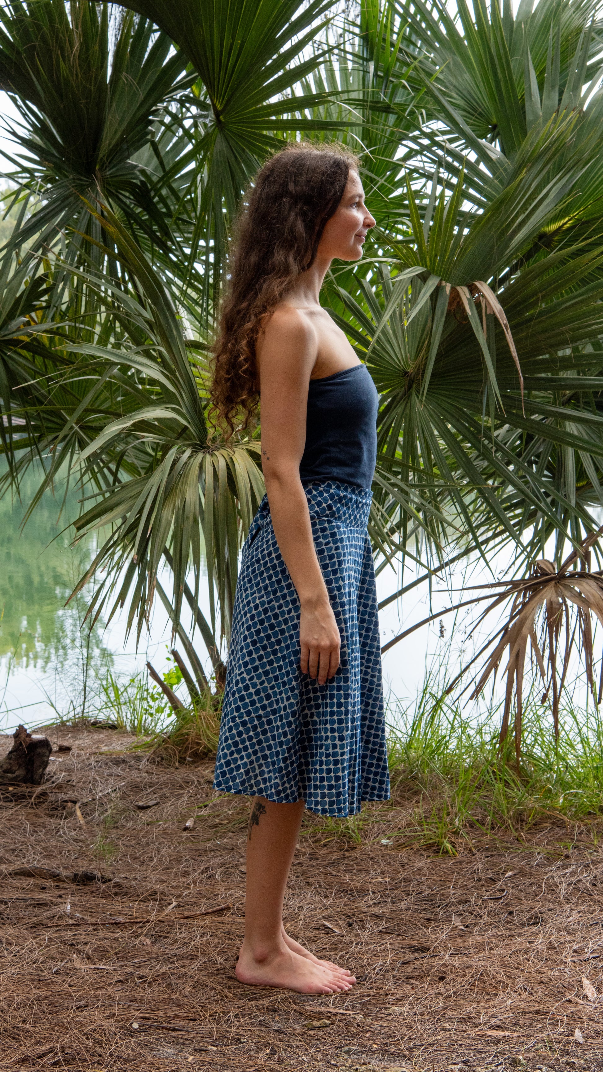 Woman in a blue dress standing in front of palm trees by a body of water