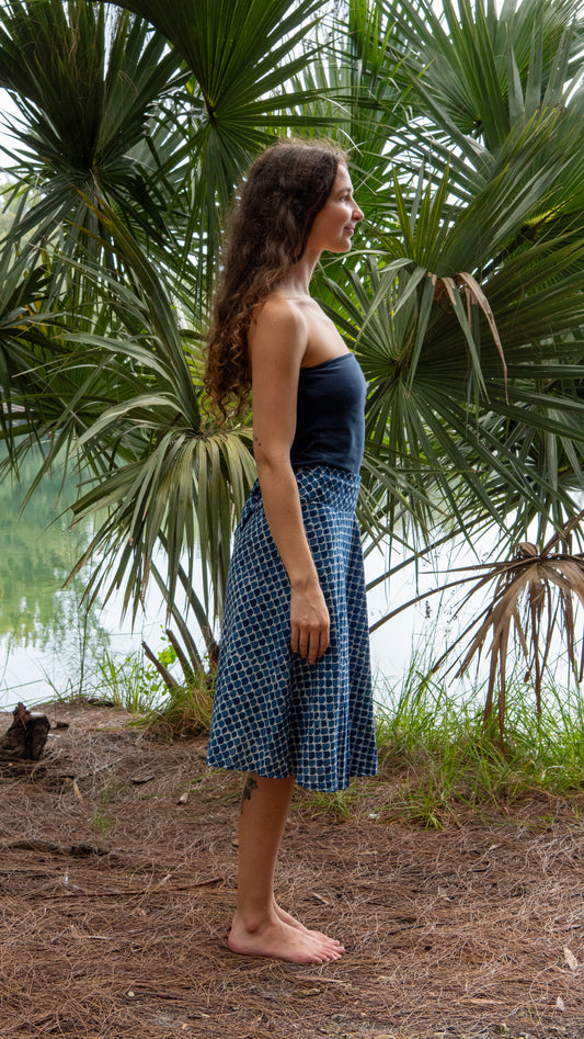 Woman in a blue dress standing in front of palm trees by a body of water