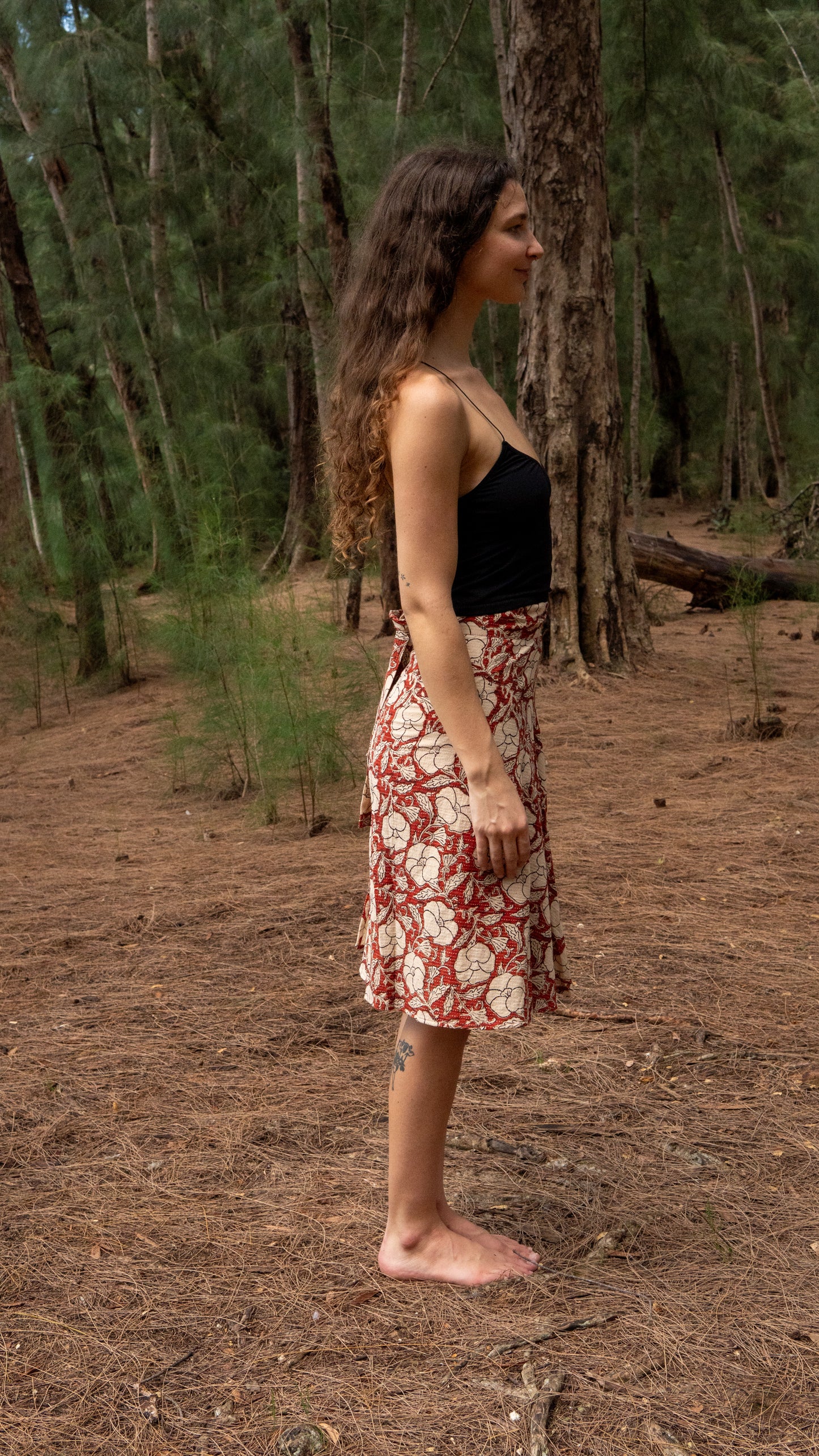 Woman standing in a forest wearing a black top and floral skirt.