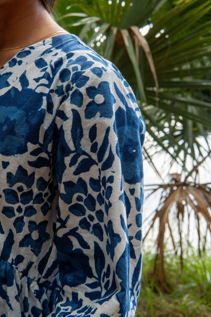 Person wearing a blue and white patterned shirt with palm leaves in the background