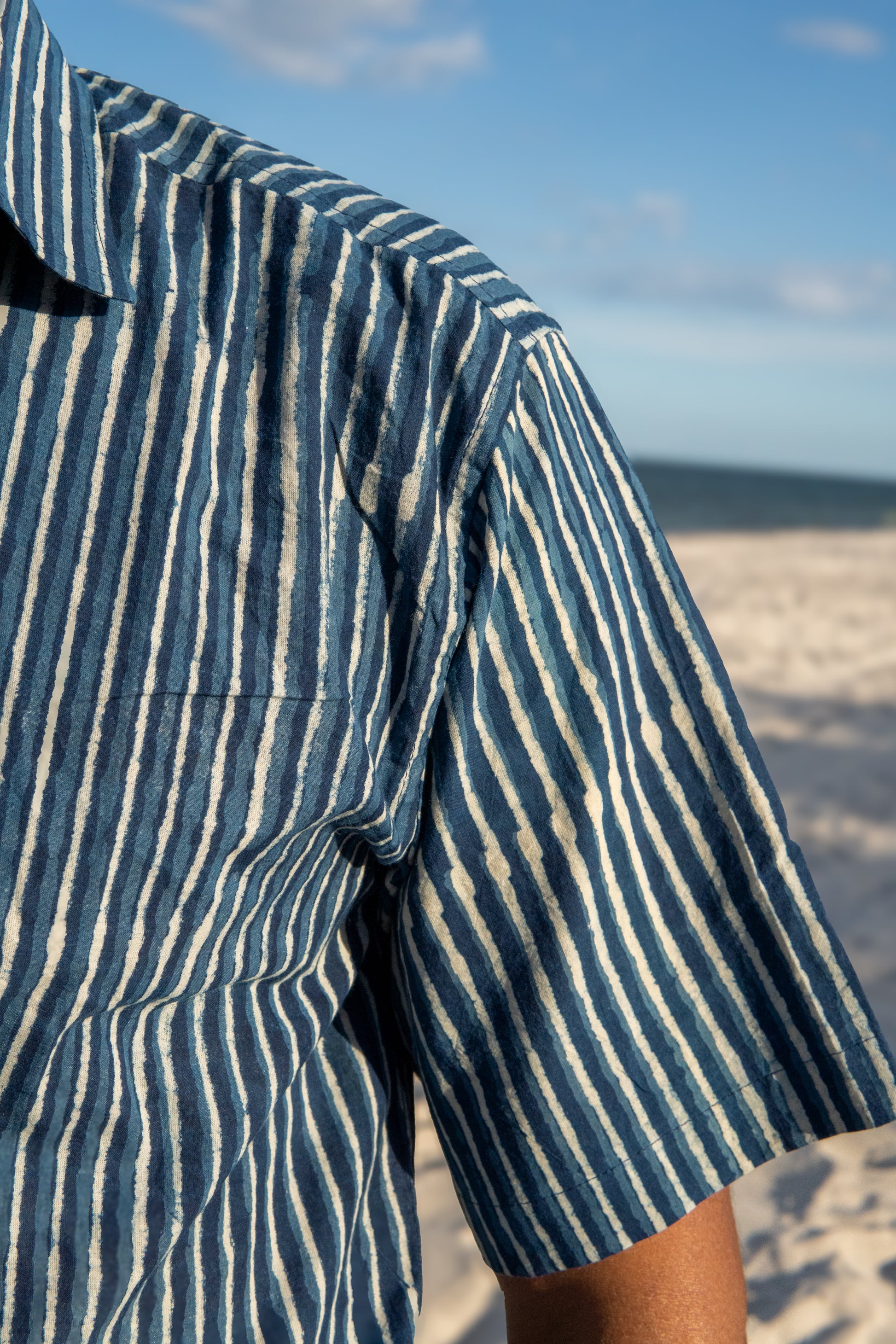 Close-up of a person wearing a blue and white striped shirt on a beach.