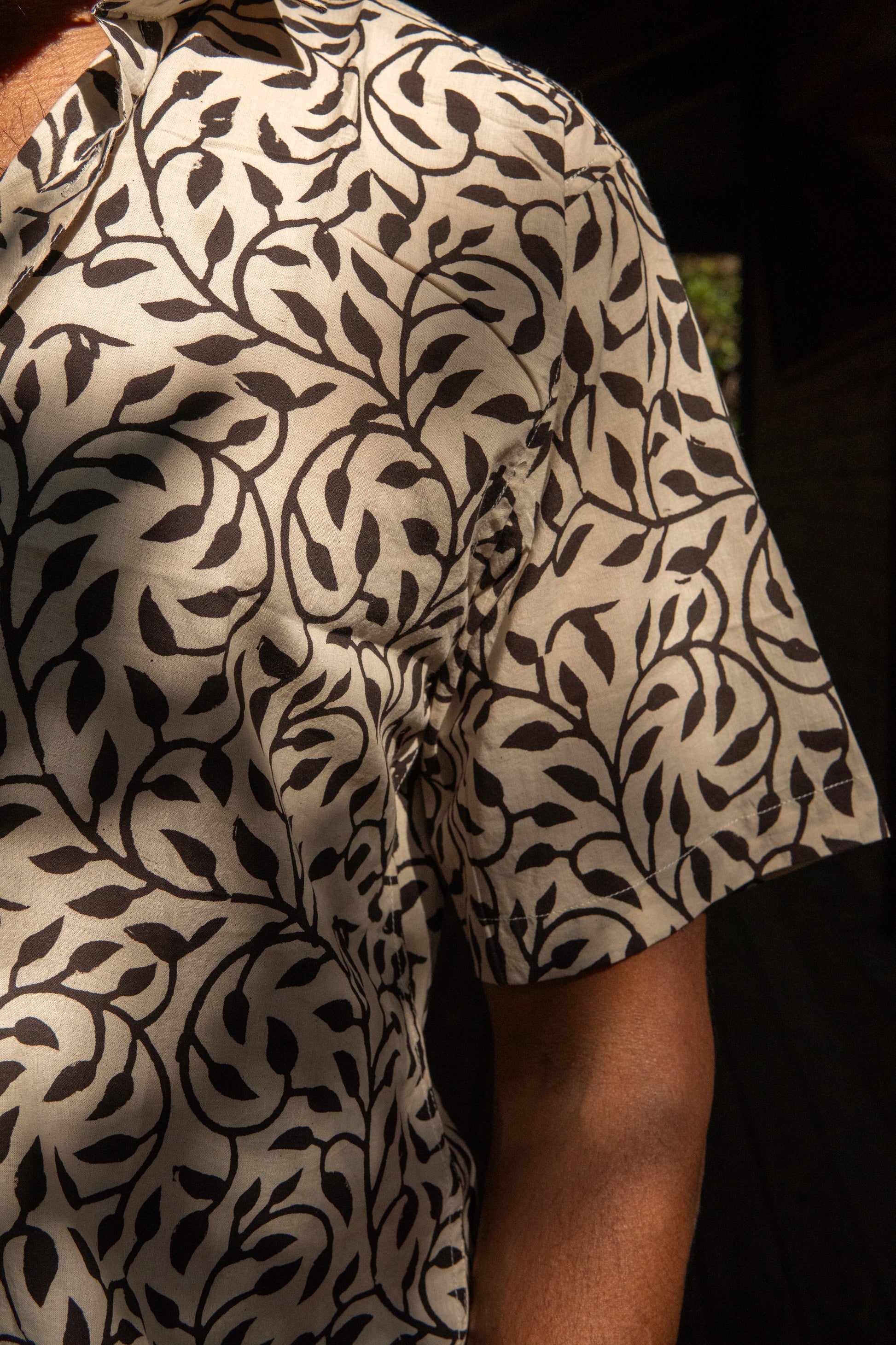Close-up of a person wearing a patterned shirt with black leaf design on a beige background.