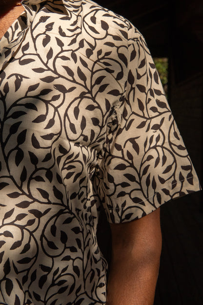 Close-up of a person wearing a patterned shirt with black leaf design on a beige background.